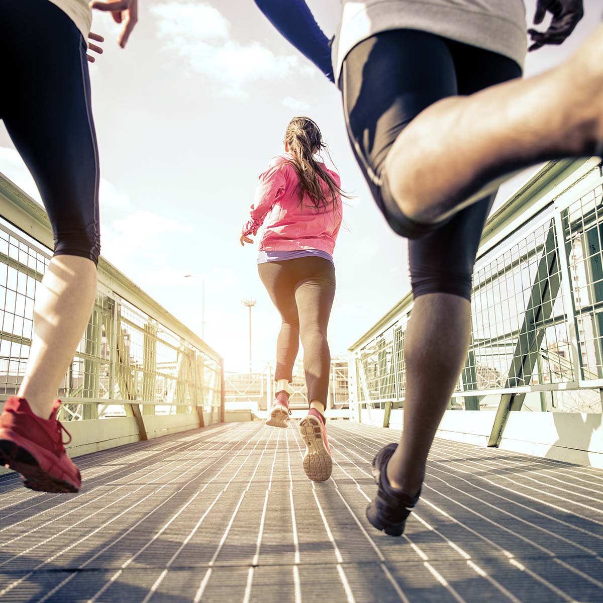 Drei Personen joggen auf einer Brücke, umgeben von einer schönen Landschaft.