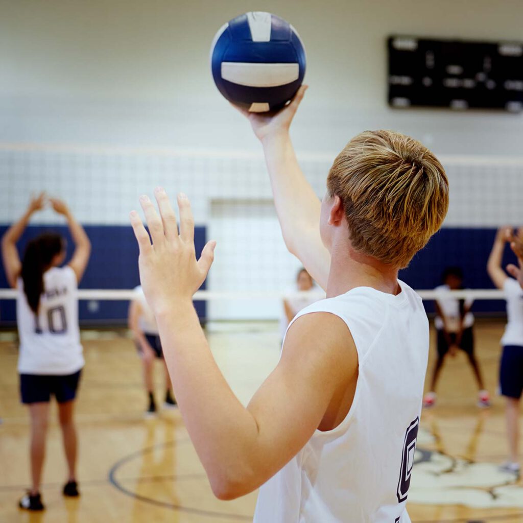 Ein junger Mann hält einen Volleyball in einer Sporthalle.