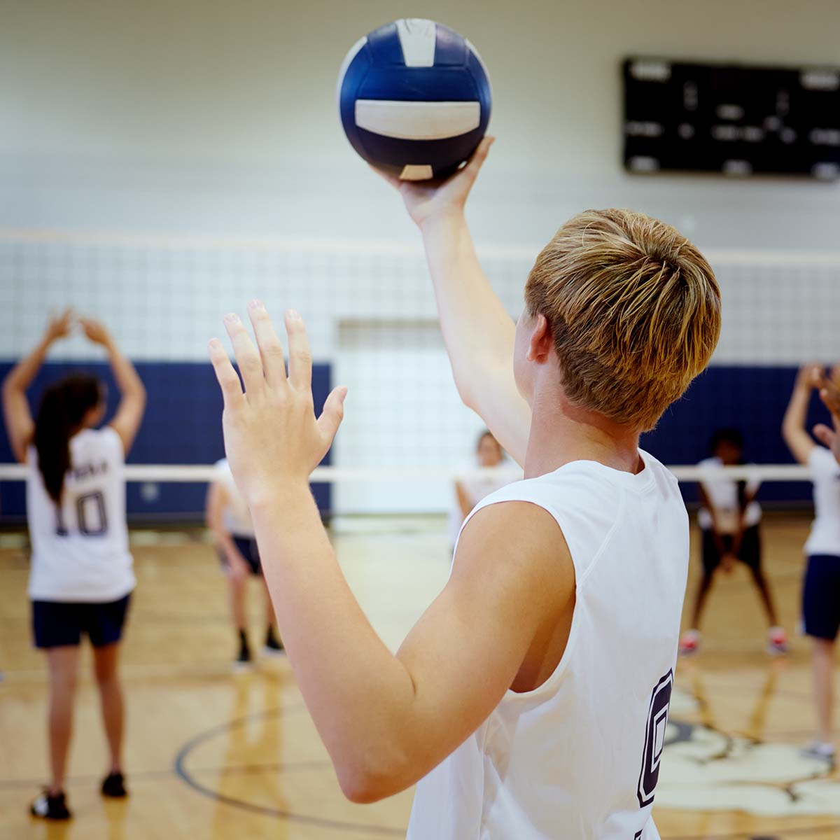 Ein junger Mann hält einen Volleyball in einer Sporthalle.